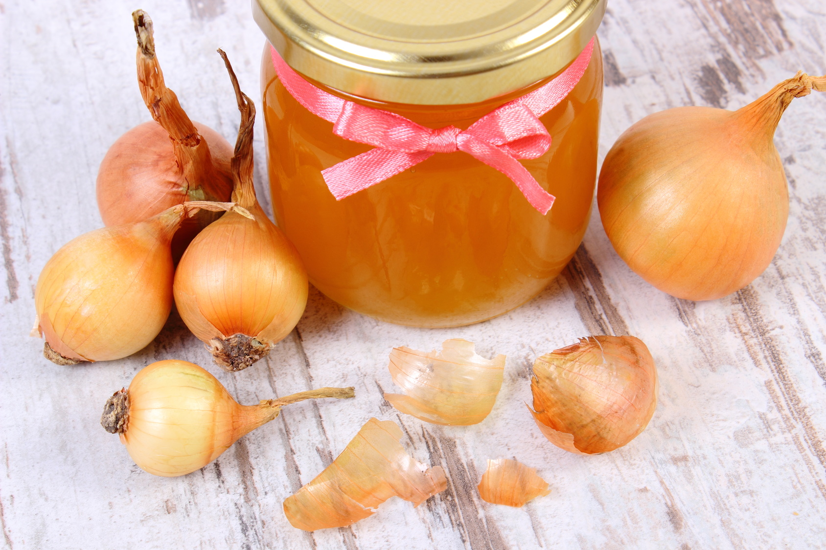 Fresh organic honey in glass jar and onions on wooden background, healthy nutrition and